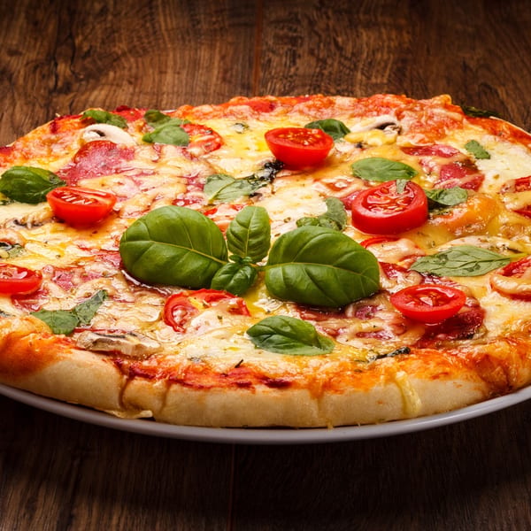 A delicious pizza with melted cheese, pepperoni, mushrooms, cherry tomatoes, and fresh basil on a wooden table.